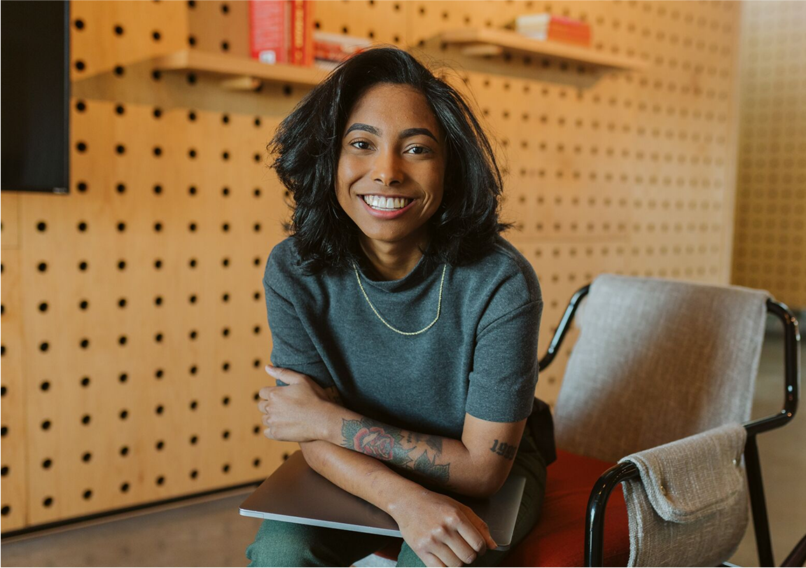 person smiling at camera with laptop in hand